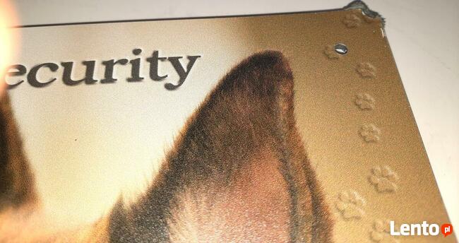 Tablica ostrzegawcza, informacyjna z owczarkiem niemieckim.