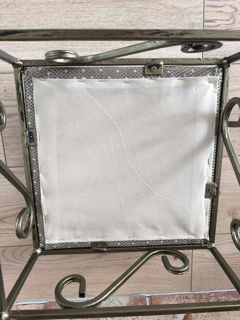 Taboret z metalowymi nogami i ozdobnikami.