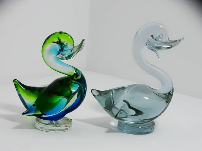 Dwie szklane figurki kaczek — jedna wielobarwna, druga w odc