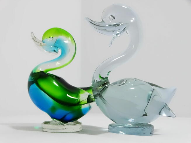Dwie szklane figurki kaczek — jedna wielobarwna, druga w odc