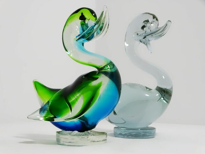 Dwie szklane figurki kaczek — jedna wielobarwna, druga w odc
